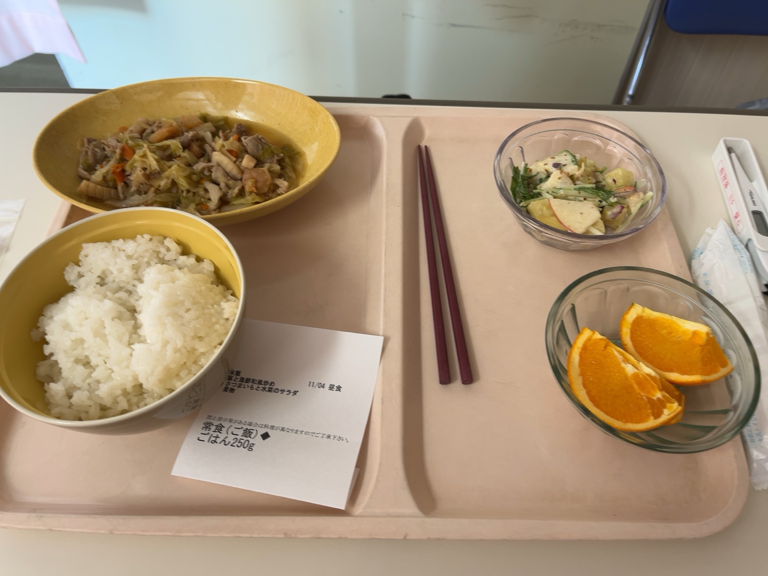 「11月4日 昼食｜鶏肉と野菜の炒め煮、りんごと水菜のサラダ、オレンジ、ご飯250g。栄養バランスの良い昼食」