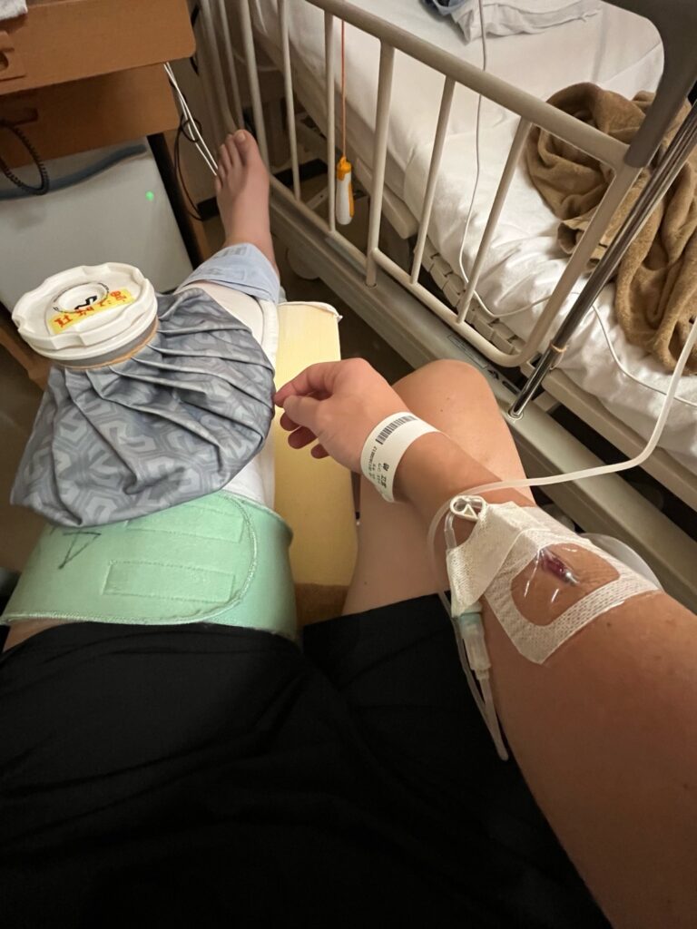 手に点滴をつけた状態でベッドに座る様子