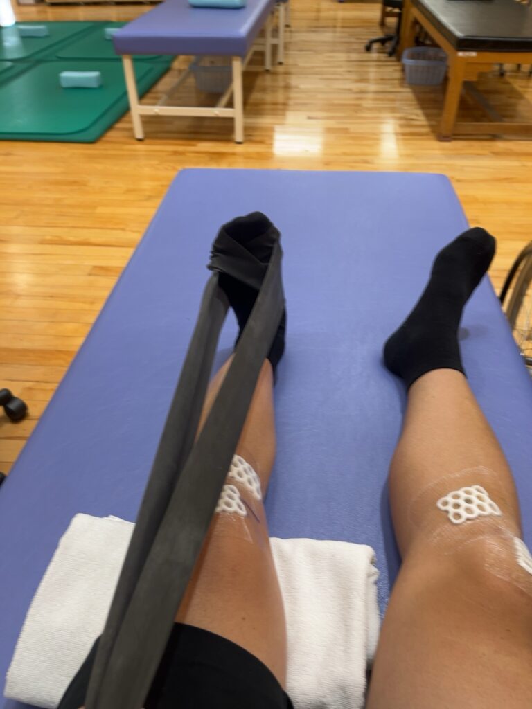 リハビリ中、チューブを足にかけて下腿の筋肉を動かすトレーニング風景(ACLリハビリ5日目)