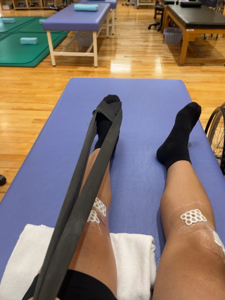 チューブを用いたリハビリで膝下の可動域を広げるトレーニング中の様子（ACLリハビリ7日目）